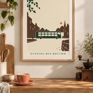 May include: A framed wall art print featuring a stylized illustration of a dark green double-decker bus on a street at dusk. The scene includes brown silhouettes of buildings, a small red sun, and tree branches. The text reads EVENING BUS RHYTHM.