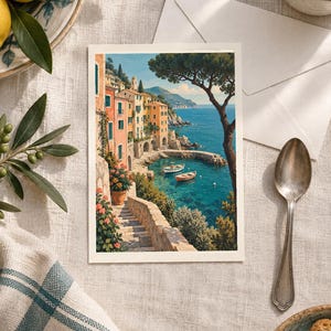 May include: A rectangular greeting card featuring a colourful illustration of a coastal Italian village with pastel buildings, stone stairs, and flowering plants overlooking a blue bay with two small boats, set against a clear sky and distant cliffs.