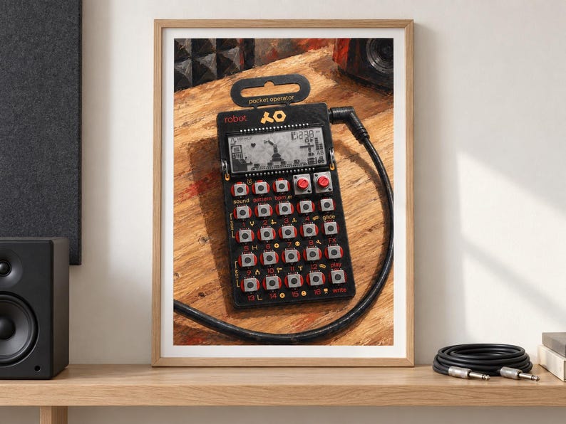 May include: A black Teenage Engineering PO-28 Robot pocket operator synthesiser featuring a monochrome LCD screen, a grid of twenty-three silver buttons with red accents, and a black audio cable plugged into the top right side of the device.