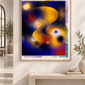 May include: A framed rectangular wall art print featuring an abstract composition with a central, fluid, golden-yellow organic shape set against a deep blue, spray-painted background with scattered yellow, red, and white speckles and light spots.