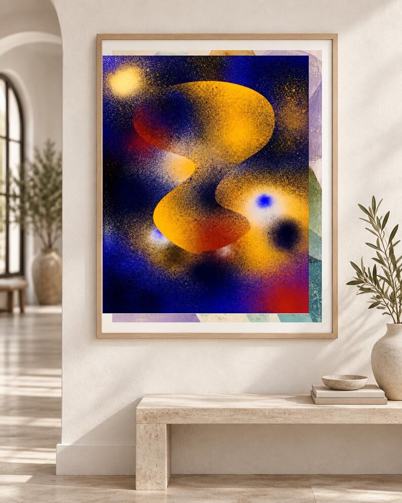 May include: A framed rectangular wall art print featuring an abstract composition with a central, fluid, golden-yellow organic shape set against a deep blue, spray-painted background with scattered yellow, red, and white speckles and light spots.