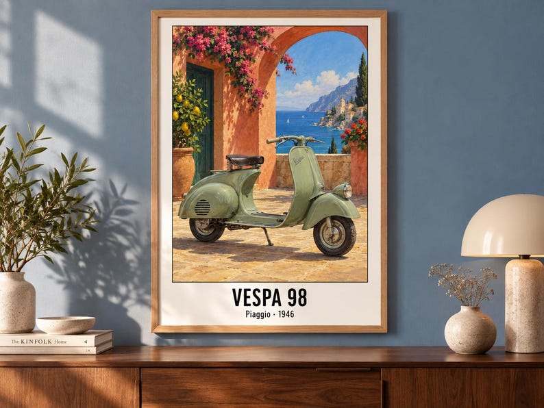 Pu&ograve; includere: Una stampa artistica incorniciata raffigurante uno scooter Vespa 98 verde salvia parcheggiato su un patio in pietra. Lo sfondo mostra una scena costiera mediterranea con un arco arancione, fiori rosa e il mare blu. Il testo recita VESPA 98 Piaggio 1946.