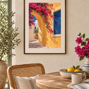 May include: A framed wall art print depicting a Mediterranean scene with a yellow stucco wall, a bright blue shuttered window, and vibrant pink bougainvillea flowers cascading over a stone archway, set in a dark brown frame with a white mat.