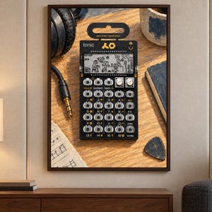 May include: A black Teenage Engineering PO-32 Tonic pocket operator synthesizer featuring a monochrome LCD screen with animated graphics, a grid of sixteen circular buttons, two silver rotary knobs, and the text pocket operator and tonic.