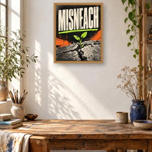 May include: A rectangular framed wall art print featuring the word MISNEACH in bold white capital letters. Below the text, a small green sprout emerges from a cracked dark gray surface, accented by vibrant orange and lime green graphic elements.