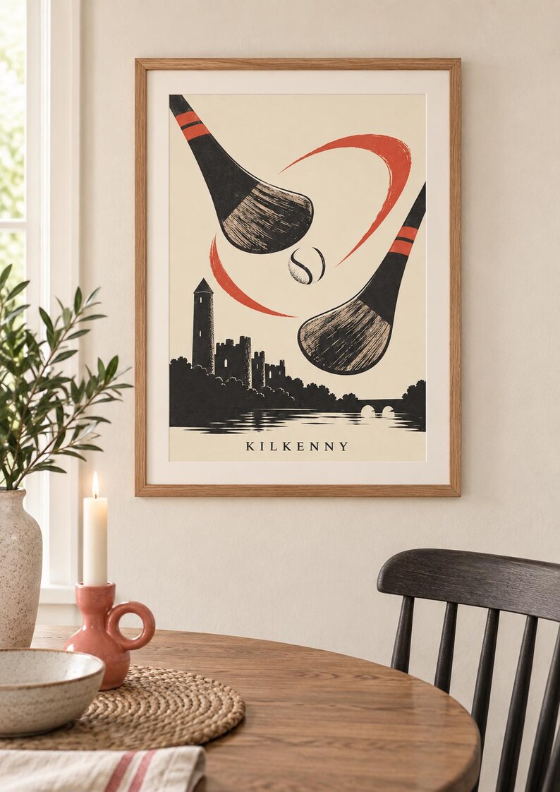 Peut inclure: Une impression d'art encadr&eacute;e pr&eacute;sentant une illustration stylis&eacute;e de deux crosses de hurling noires et d'une balle en mouvement au-dessus d'une silhouette du ch&acirc;teau et de la tour ronde de Kilkenny. Fond cr&egrave;me avec des accents rouges et le texte KILKENNY.