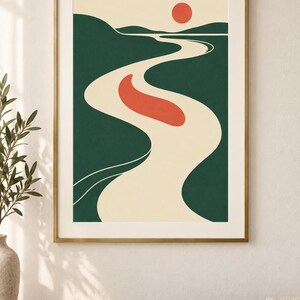 May include: A framed wall art print featuring a stylized landscape illustration with a winding cream-colored river, dark green rolling hills, a solid red sun, and a single red organic shape floating in the center of the river against a cream background.