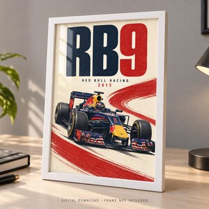 May include: A framed poster featuring a dark blue and red Formula 1 race car on a track. The text reads RB9, RED BULL RACING, and 2013. The design includes a bold red curved brushstroke across a cream background, showcasing the car in motion.