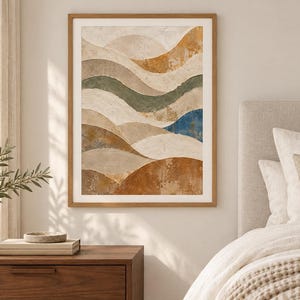 Pu&ograve; includere: Una stampa artistica da parete incorniciata che presenta una composizione paesaggistica astratta con forme curve stratificate in tonalit&agrave; terracotta, beige, verde salvia e un singolo accento blu intenso, in una cornice di legno chiaro.