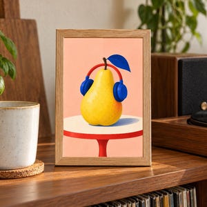 May include: A rectangular wooden frame containing a print of a yellow pear wearing blue headphones. The pear sits on a small white table with a red base against a light peach background. The illustration features a single dark blue leaf on top.