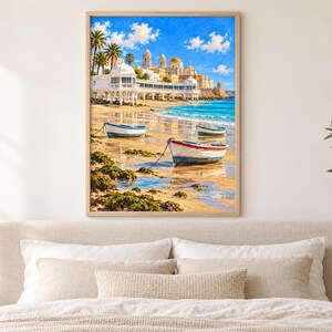 Op de afbeelding: Een ingelijste kunstdruk met een kusttafereel met drie kleine boten op een zandstrand. Op de achtergrond staat een wit gebouw met een koepeldak langs de kustlijn onder een helderblauwe lucht met verspreide witte wolken.