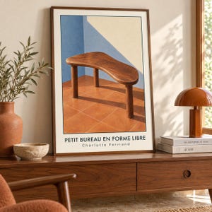 May include: A framed art print featuring a wooden table with a free-form top and three cylindrical legs. The background shows a blue and cream wall above a terracotta tiled floor. The text PETIT BUREAU EN FORME LIBRE Charlotte Perriand is printed below.