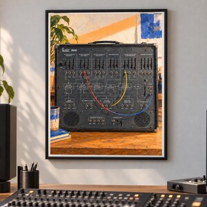 May include: A framed wall print depicting a vintage ARP 2600 analog synthesizer. The black control panel features numerous sliders, knobs, and patch points connected by red, yellow, and blue patch cables, with a handle on top of the unit.