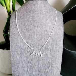 May include: A silver necklace with a silver pendant shaped like a chemical molecule. The necklace is displayed on a grey mannequin.