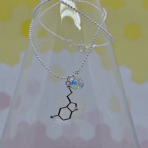 May include: A silver-toned ball chain necklace featuring a pendant shaped like a chemical molecular structure. The pendant is accompanied by a small, round, iridescent crystal charm that reflects multiple colors, attached to the same silver jump ring.