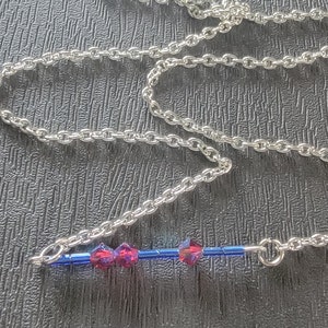 May include: A silver chain necklace with a blue and red beaded pendant. The pendant has four red beads and a blue bar in the center.