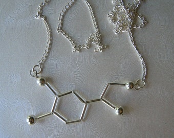 May include: A silver necklace with a pendant shaped like the chemical structure of dopamine. The pendant is made of small silver tubes and beads.