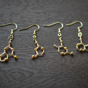 Könnte beinhalten: Vier Paar goldene Ohrringe mit einem chemischen Strukturdesign. Die Ohrringe bestehen aus kleinen goldenen Perlen, die zu einer geometrischen Form verbunden sind.