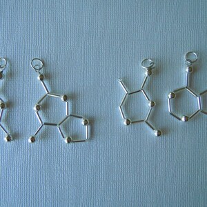 Könnte beinhalten: Vier silberne Metallanhänger in Form einer chemischen Struktur mit einer Öse oben zum Aufhängen.