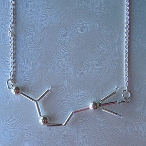 May include: A silver necklace with a pendant shaped like a chemical molecule. The pendant is made of small silver balls connected by thin silver rods.