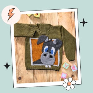 May include: A green knitted sweater with a cartoon donkey appliqué on the front. The donkey has blue eyes and a gray nose. The sweater is on a wooden surface with some wooden blocks.