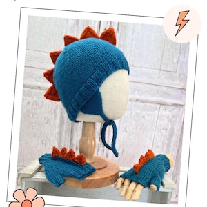 May include: A teal knitted hat with earflaps and orange triangular spikes along the back, paired with matching fingerless gloves that feature similar orange spikes on the top. The set is displayed on a mannequin head and wooden hand form.