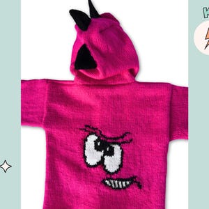 May include: A vibrant pink knitted hoodie with a cartoon face design. The hood has black horns and the face features white eyes, a black mouth, and a grumpy expression. The word "KNIT" is in a circle with a lightning bolt.