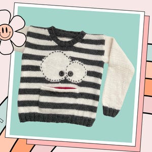 May include: A striped knit sweater with a white and gray color scheme. The sweater has a whimsical face design with a pocket on the front. The sweater is made of soft, comfortable yarn.