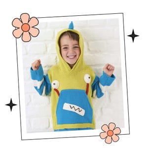 May include: A child wearing a yellow and blue knitted hoodie with a monster design. The hoodie has a blue pocket with a white stitched design and two large eyes with red pupils. The child is smiling and has a happy expression.
