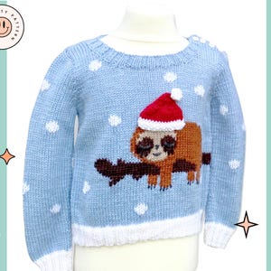 Könnte beinhalten: Ein hellblauer Strickpullover mit weißem Saum und weißen Punkten. Ein brauner Faultier, das eine rote Weihnachtsmütze trägt, ist auf der Vorderseite des Pullovers gestickt. Der Pullover trägt auf der rechten Seite des Bildes den Schriftzug "Sleepy Sloth Kids Sweater".