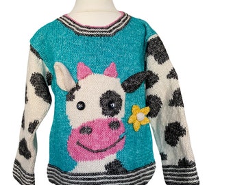 May include: A turquoise blue knitted sweater with a white and black cow design on the front. The cow has a pink nose and black eyes. The sweater has a black and white striped band around the neck and cuffs.