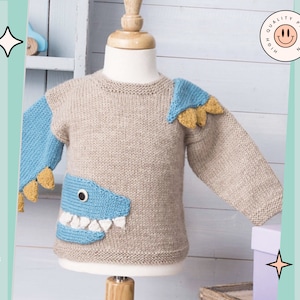 May include: A beige knitted sweater with a blue and yellow dinosaur design. The sweater has a round neckline and long sleeves. The dinosaur design is on the front and one sleeve. The sweater is on a mannequin.