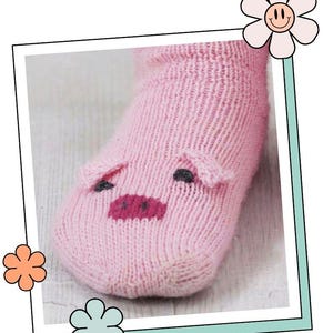 Puede incluir: Un calcetín tejido de color rosa claro con un diseño de cara de cerdo en la zona de los dedos. La cara del cerdo incluye dos pequeñas orejas que sobresalen, dos ojos oscuros y un hocico rosa oscuro. El calcetín está en un marco con flores.