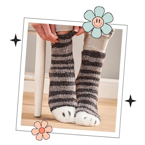 Könnte beinhalten: Paar kuschelige gestreifte Socken mit flauschigen Zehen in Pfotenform. Die Socken sind grau und schwarz mit einem weißen Pfotenabdruck an jedem Zeh.