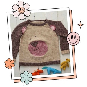 May include: A knitted brown and beige sweater with a pink bear face on the front. The sweater has brown sleeves and a beige body.