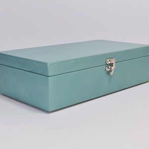 Può includere: Una scatola di legno blu chiaro con una chiusura argentata. La scatola è chiusa.