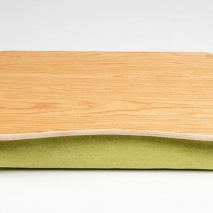 Puede incluir: Una bandeja de madera para portátil con un cojín de tela verde. La bandeja está hecha de madera clara con un patrón de veta natural. El cojín es suave y cómodo, y la bandeja es perfecta para trabajar o relajarse en la cama.