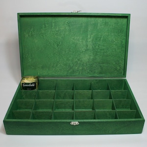 Op de afbeelding: Open, groene houten kist met meerdere compartimenten, ideaal voor het organiseren van kleine items. De kist heeft een scharnierend deksel en een zilveren sluiting. Een klein potje met het label "Greenfield" staat erin.