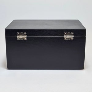 May include: A black wooden box with silver hinges. The box is closed and the lid is facing up.