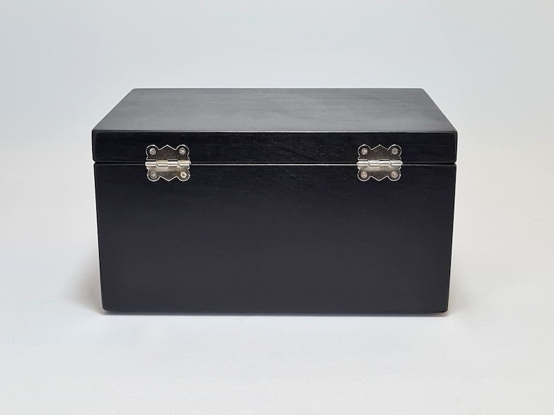 May include: A black wooden box with silver hinges. The box is closed and the lid is facing up.