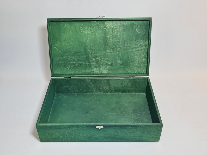 May include: An empty green wooden box with a hinged lid and a silver latch. The box is open and the inside is visible.