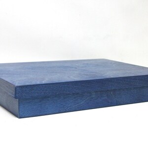 May include: A blue wooden box with a lid. The box is made of a light blue wood with a grainy texture.