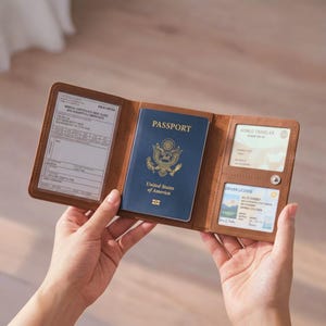 May include: A tan leather tri-fold travel wallet holding a blue United States of America passport in the center, a medical certificate in the left clear window, and a World Traveler card and driver license in the two right-side clear windows.