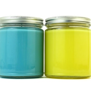 May include: Two glass candle jars with silver lids. The candle on the left is a teal blue color. The candle on the right is a bright yellow color.