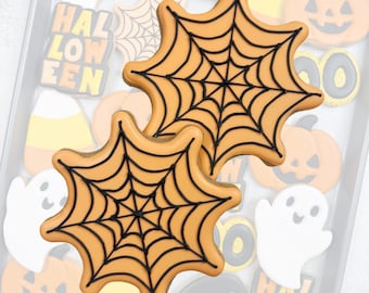 May include: Two orange spiderweb-shaped sugar cookies with black icing details layered over a tray of assorted Halloween-themed cookies, including ghosts, pumpkins, candy corn, witch hats, and text reading BOO and HALLOWEEN.