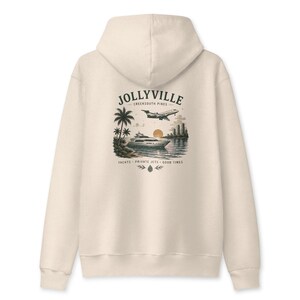 May include: A cream-colored hooded sweatshirt featuring a back graphic of a yacht, a private jet, palm trees, and a city skyline. The text reads JOLLYVILLE CREEKSOUTH PINES and YACHTS PRIVATE JETS GOOD TIMES with a small pinecone icon at the bottom.