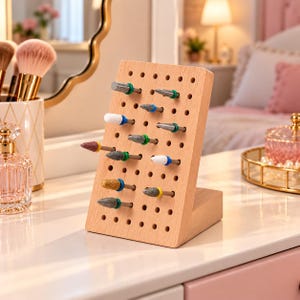 May include: A light-colored wooden pegboard stand featuring a grid of holes, holding twelve assorted metal and ceramic nail drill bits. Each bit is equipped with a small colored rubber ring at the base, including green, blue, white, and yellow accents.