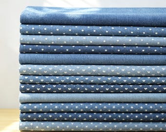 Könnte beinhalten: Ein Stapel gefalteter Stoffstücke in verschiedenen Blautönen. Die Sammlung umfasst einfarbige Texturen in Denim-Optik, weiße Punkte, kleine weiße Herzmuster und weiße Sternmotive, die ordentlich in einem vertikalen Stapel angeordnet sind.