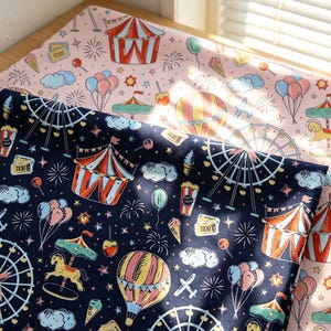 May include: Two pieces of fabric featuring a carnival theme. One piece is light pink and the other is dark navy blue. Both fabrics are printed with illustrations of circus tents, ferris wheels, hot air balloons, carousels, balloons, and tickets.
