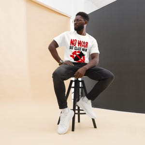 May include: A white short-sleeved t-shirt featuring the red text NO WAR with a black line through it, followed by the black text BUT CLASS WAR, and a red circular symbol containing a black bomb graphic and a crossed-out hammer and sickle.